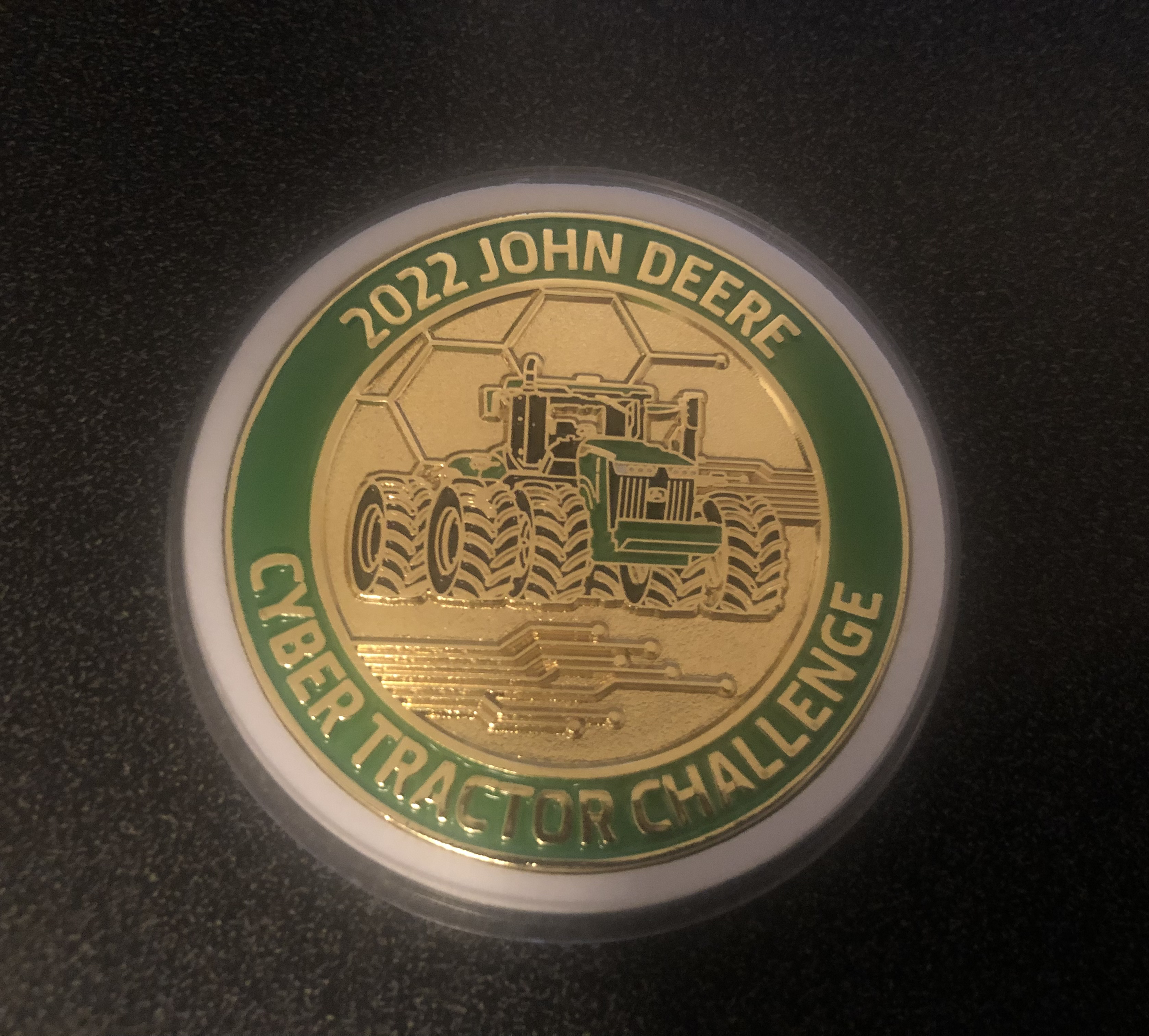 Image of gold and green coin with "2022 John Deere Cyber Tractor Challenge" along the circumference of the coin, and a large tractor with circuit themed background in the center of the coin